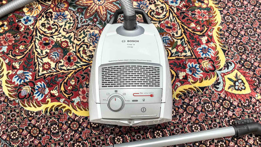 Ein weißer Staubsauger auf einem Perserteppich. Blog-Beitrag: Wie pflege ich handgeknüpfte Teppiche richtig? © Daniel Khademi, JUPITER Intl.