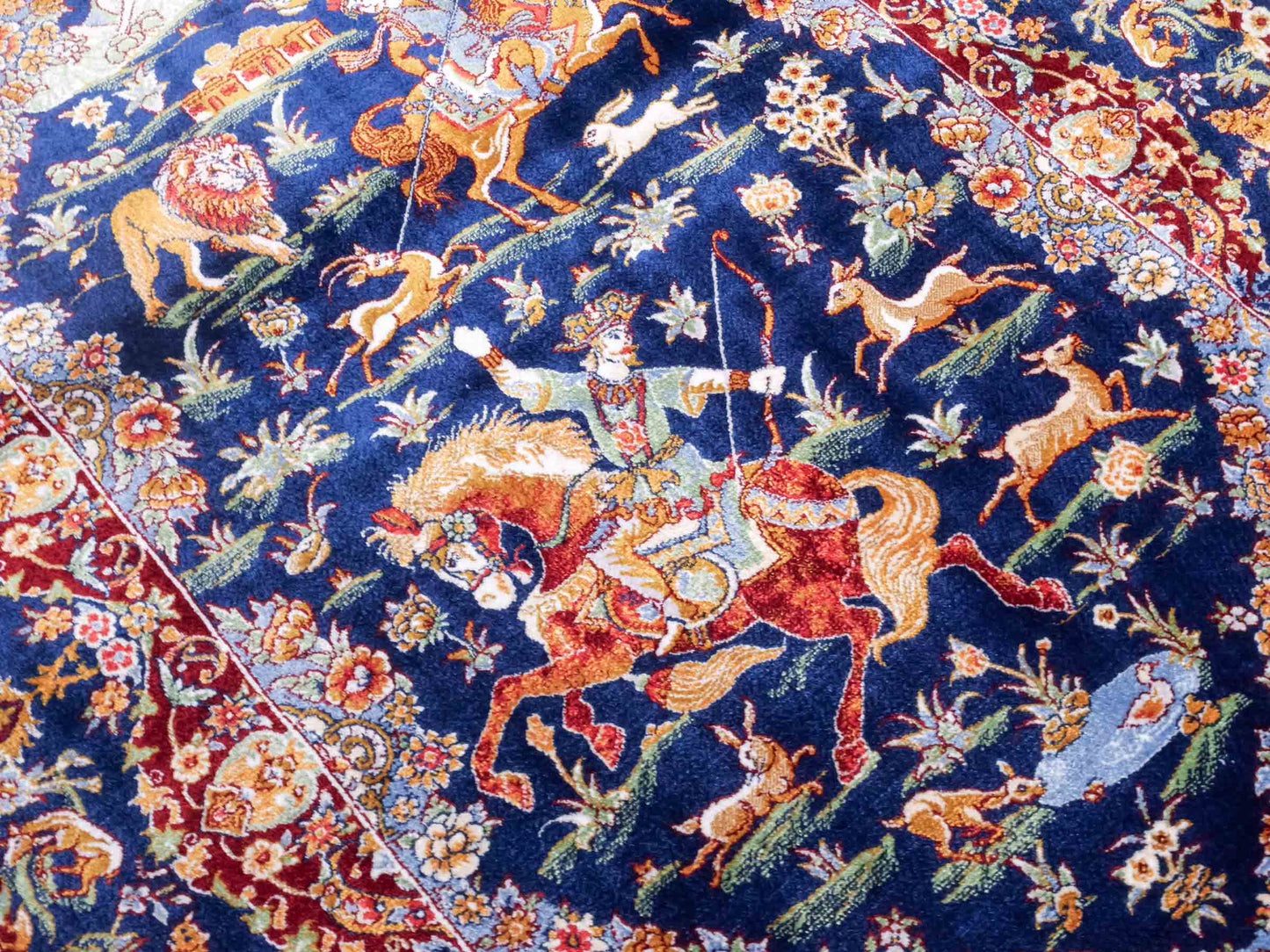 Ghom Maschinenteppich "Banu" 90 x 60 cm aus pflanzlicher Seide (Viskose) mit Jagdmotiv, Marineblau. Teppichnummer: V13NY054H. Persian Luxury Collection by Khademi. Made in Iran / Persia – Vertrieb durch JUPITER Intl.