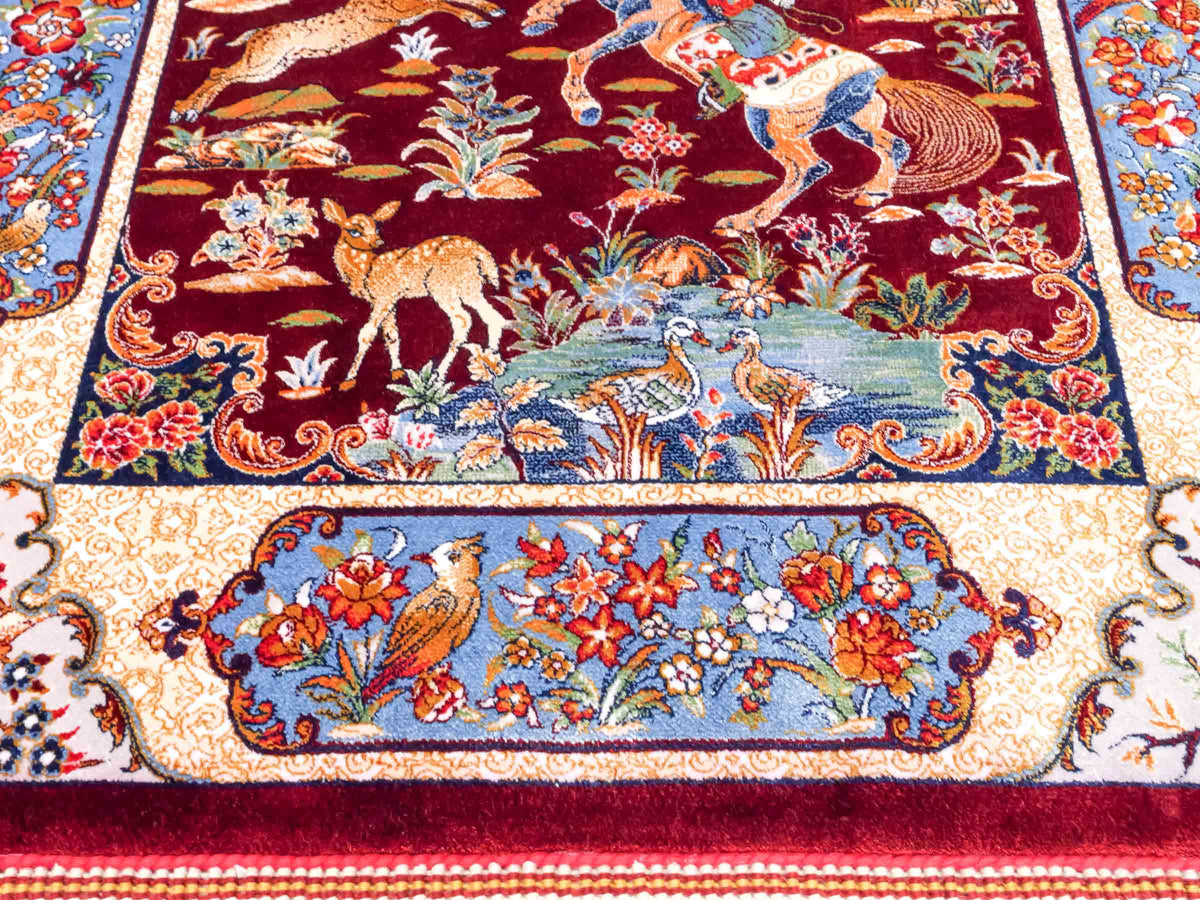 Ghom Maschinenteppich "Fariborz" 90 x 60 cm, mit Jagdmotiv, Rot-Blau, aus pflanzlicher Seide (Viskose), Hand-Finished. Teppichnummer: V25RL054H. Persian Luxury Collection by Khademi. Made in Iran / Persia – Vertrieb durch JUPITER Intl.