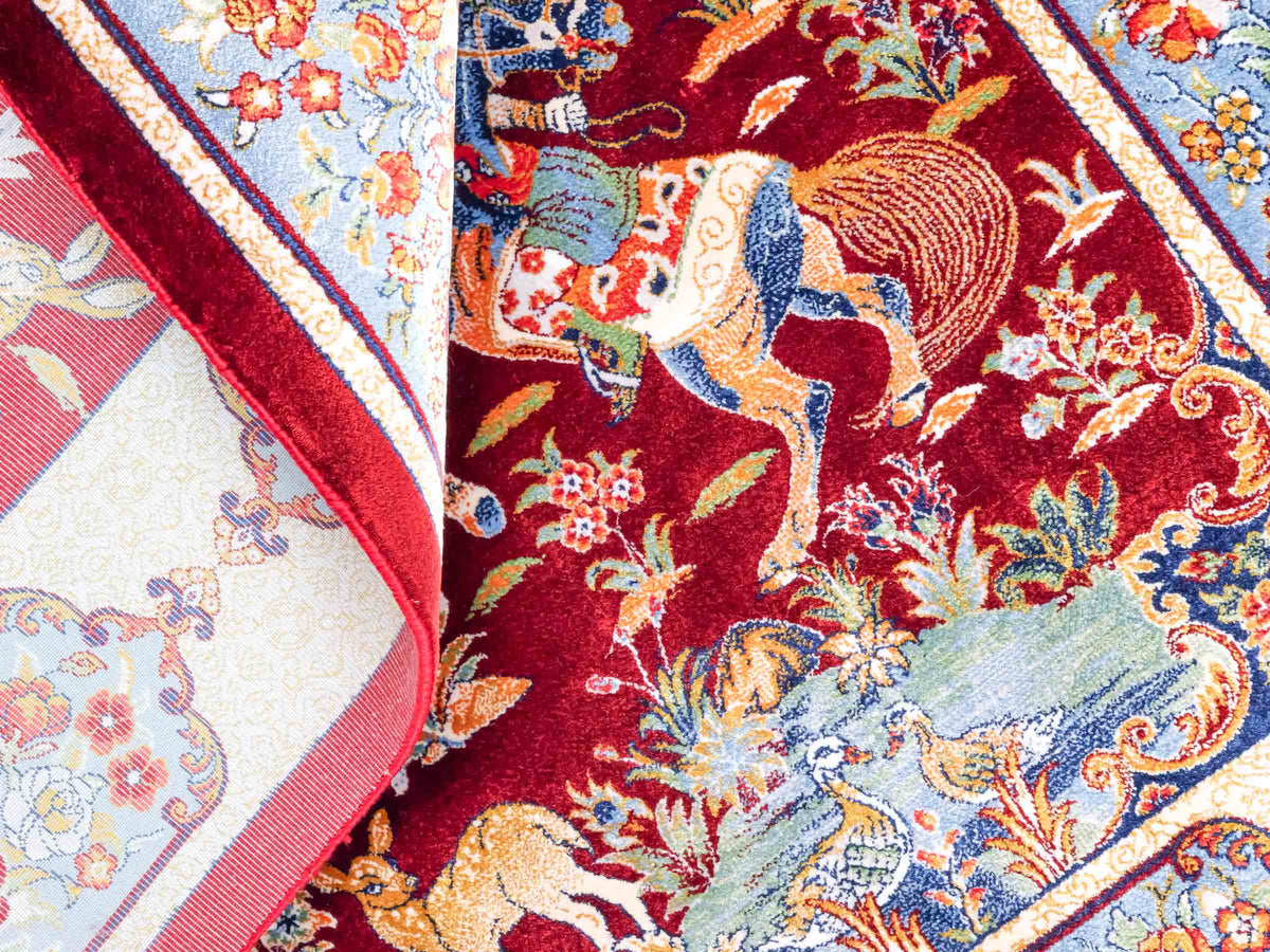 Ghom Maschinenteppich "Fariborz" 90 x 60 cm, mit Jagdmotiv, Rot-Blau, aus pflanzlicher Seide (Viskose), Hand-Finished. Teppichnummer: V25RL054H. Persian Luxury Collection by Khademi. Made in Iran / Persia – Vertrieb durch JUPITER Intl.