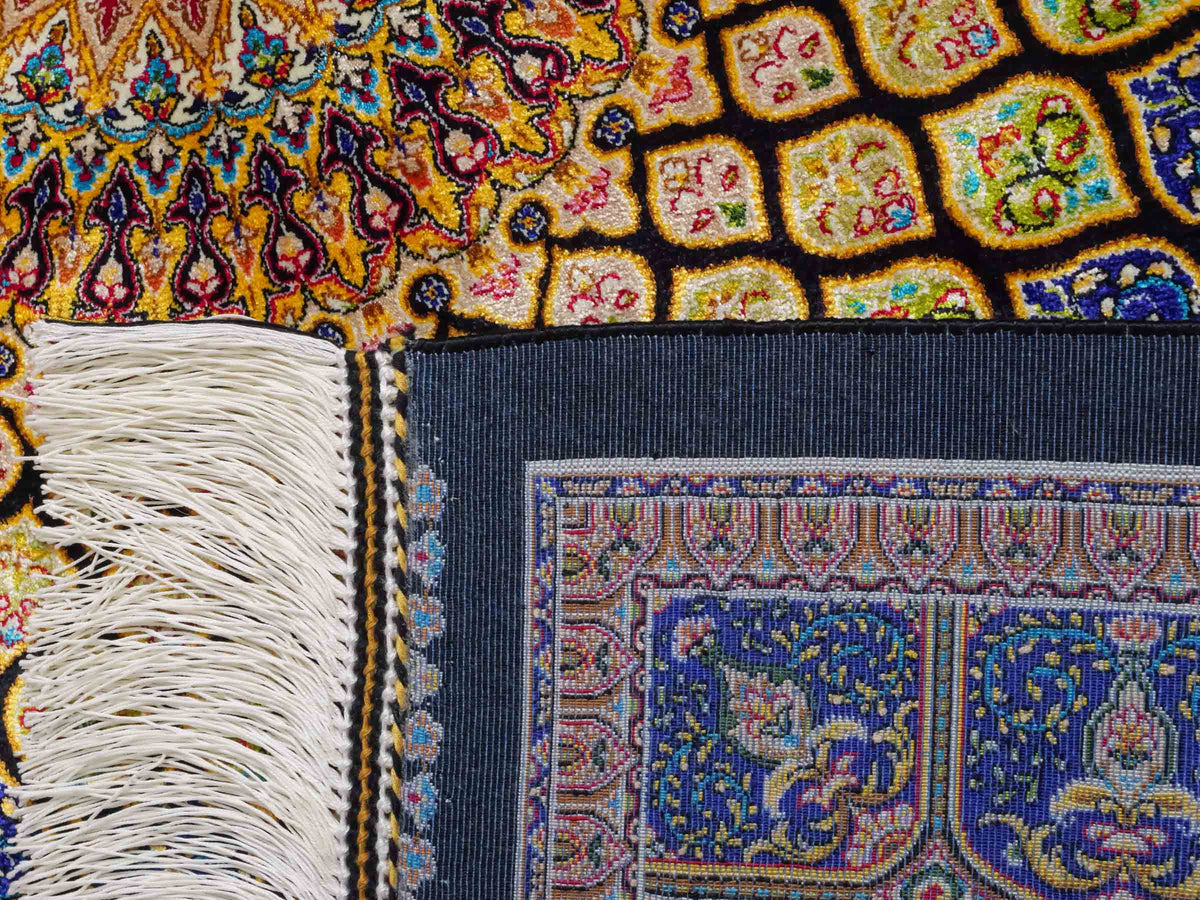 Ghom Maschinenteppich "Manuchehr" 150 x 100 cm, mit Medaillon, aus pflanzlicher Seide (Viskose), Schwarz/Blau/Gold. Teppichnummer: V56BD150H. Persian Luxury Collection by Khademi. Made in Iran / Persia – Vertrieb durch JUPITER Intl.