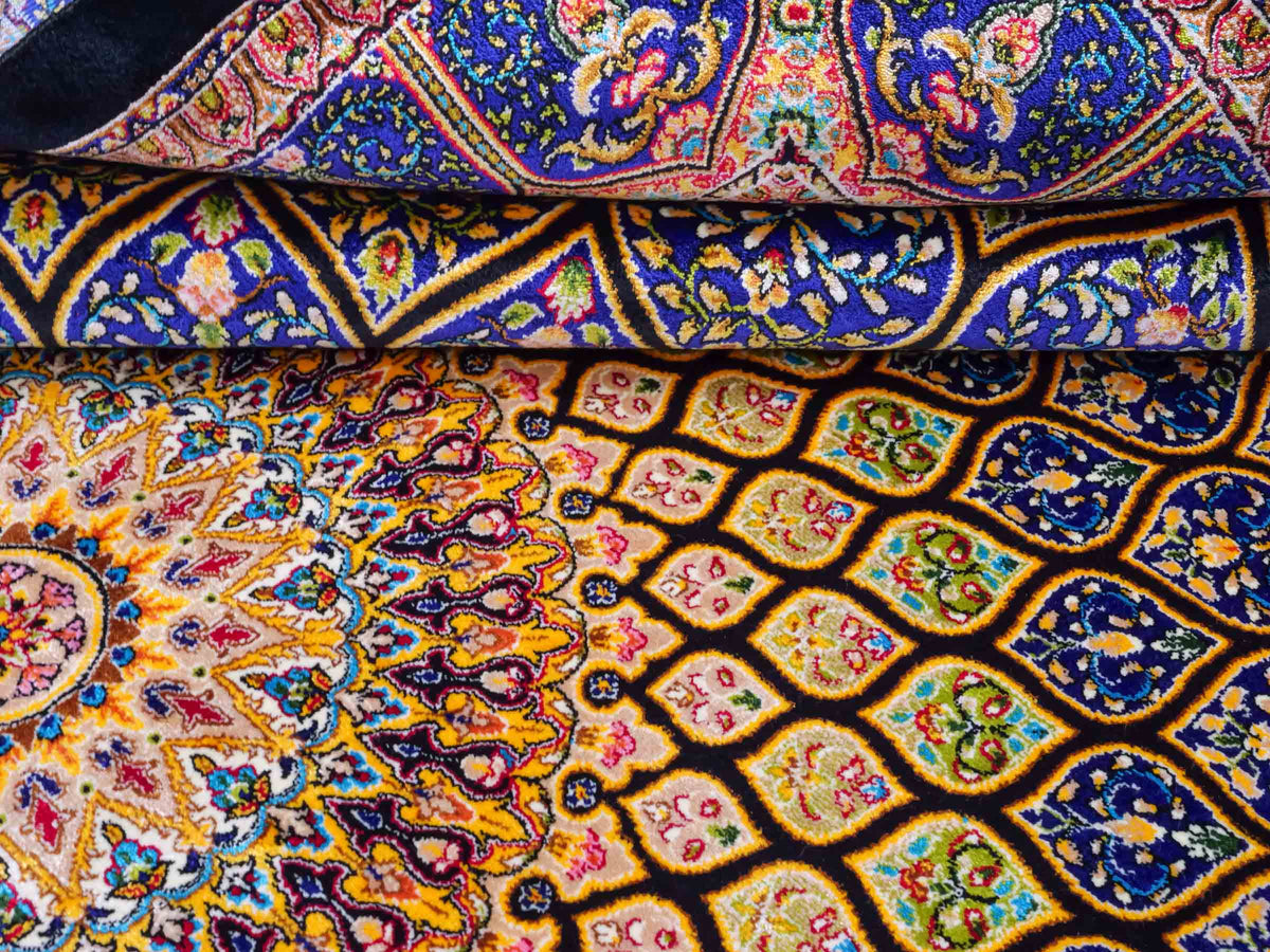Ghom Maschinenteppich "Manuchehr" 150 x 100 cm, mit Medaillon, aus pflanzlicher Seide (Viskose), Schwarz/Blau/Gold. Teppichnummer: V56BD150H. Persian Luxury Collection by Khademi. Made in Iran / Persia – Vertrieb durch JUPITER Intl.