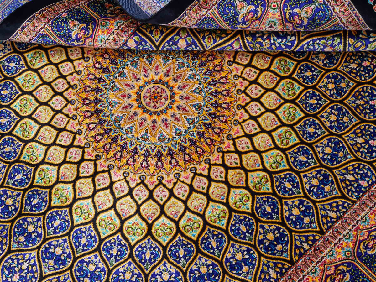 Ghom Maschinenteppich "Manuchehr" 150 x 100 cm, mit Medaillon, aus pflanzlicher Seide (Viskose), Schwarz/Blau/Gold. Teppichnummer: V56BD150H. Persian Luxury Collection by Khademi. Made in Iran / Persia – Vertrieb durch JUPITER Intl.