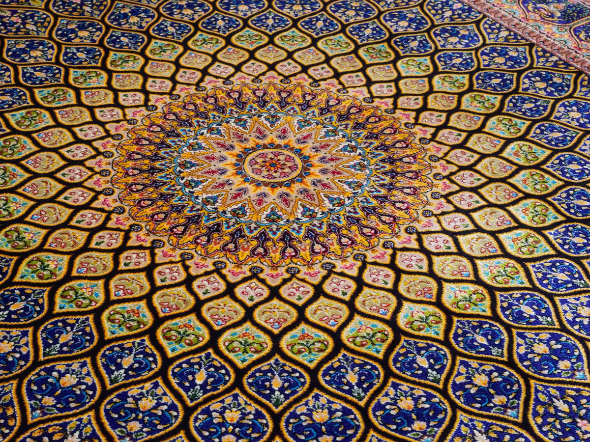 Ghom Maschinenteppich "Manuchehr" 150 x 100 cm, mit Medaillon, aus pflanzlicher Seide (Viskose), Schwarz/Blau/Gold. Teppichnummer: V56BD150H. Persian Luxury Collection by Khademi. Made in Iran / Persia – Vertrieb durch JUPITER Intl.