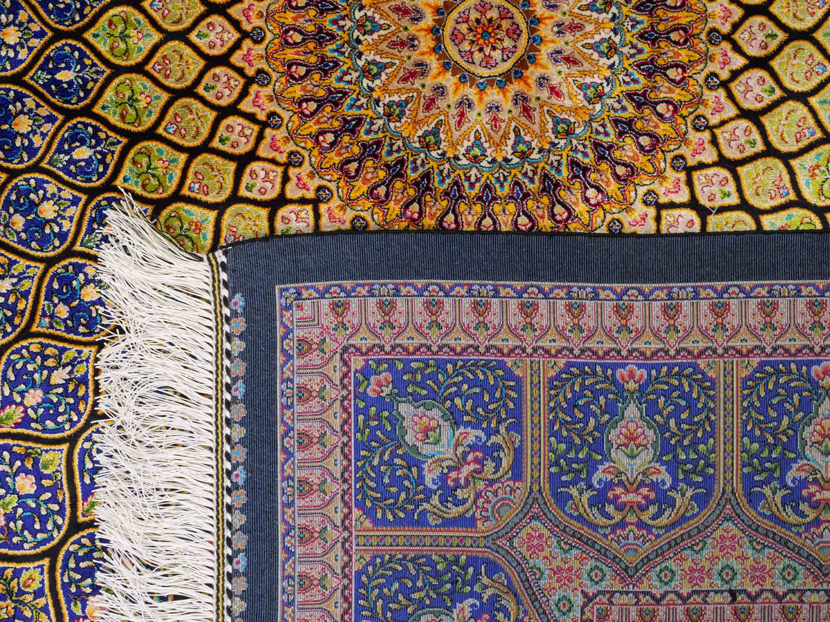 Ghom Maschinenteppich "Manuchehr" 225 x 150 cm, mit Medaillon, aus pflanzlicher Seide (Viskose), Schwarz/Blau/Gold. Teppichnummer: V56BD338H. Persian Luxury Collection by Khademi. Made in Iran / Persia – Vertrieb durch JUPITER Intl.