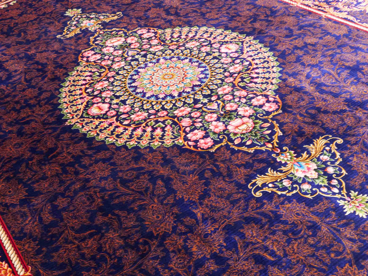 Ghom Maschinenteppich "Piruz" 225 x 150 cm, mit Medaillon, aus pflanzlicher Seide (Viskose), Marineblau/Orange/Gold. Teppichnummer: V69NY338H. Persian Luxury Collection by Khademi. Made in Iran / Persia – Vertrieb durch JUPITER Intl.