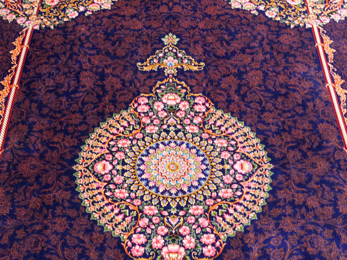 Ghom Maschinenteppich "Piruz" 225 x 150 cm, mit Medaillon, aus pflanzlicher Seide (Viskose), Marineblau/Orange/Gold. Teppichnummer: V69NY338H. Persian Luxury Collection by Khademi. Made in Iran / Persia – Vertrieb durch JUPITER Intl.